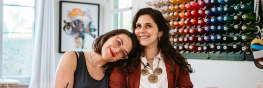 two ladies in front of a wall of colorful thread with the one on the left leaning on the one of the right psychic stitch